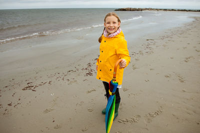 Full length portrait of girl holding umbrella while standing at beach