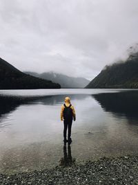Full length of person with backpack standing in lake against sky