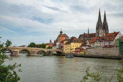 Arch bridge over river by buildings against sky