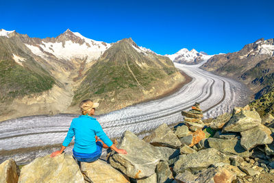 Rear view of woman sitting on rock in against mountain range