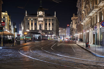 Illuminated railroad tracks amidst buildings in city at night