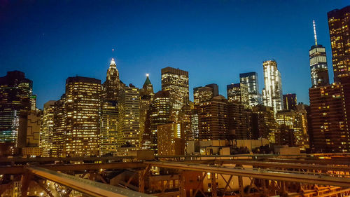 Illuminated cityscape against clear blue sky at night