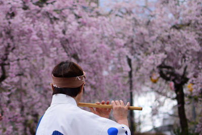 Rear view of man holding pink cherry blossom