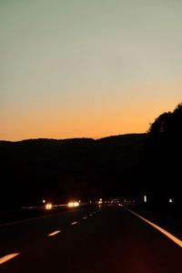 Silhouette city street against sky during sunset