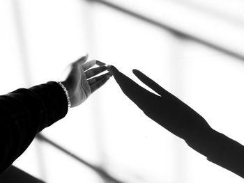 Cropped hand of woman touching shadow on wall