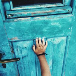 Close-up of hand touching closed blue door