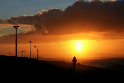 Silhouette person by sea against cloudy sky during sunset