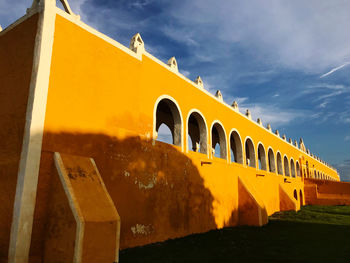 Low angle view of yellow fort against cloudy sky