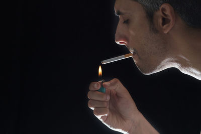 Close-up of man igniting cigarette against black background