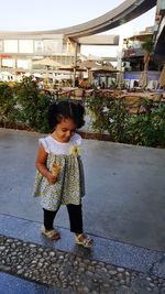 Cute girl holding ice cream cone standing against plants in city