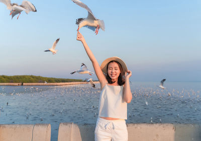 Smiling woman feeding seagull against clear sky