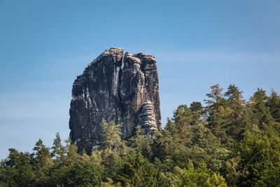 Low angle view of rock formation amidst trees against sky