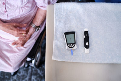 Top view of crop anonymous elderly female sitting in wheelchair near table with special glucose meter in light room at home