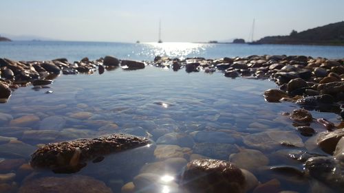 Pebbles in sea against sky on sunny day