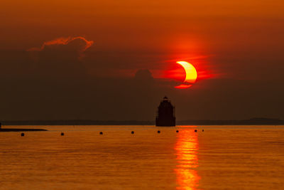 Silhouette building by sea against romantic sky at sunset