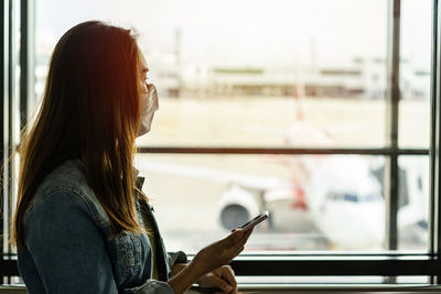 Side view of young woman using phone on window