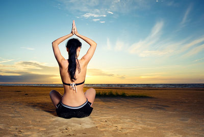 Woman practicing yoga at beach during sunset