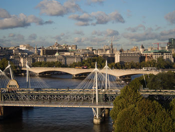 Bridge over river by buildings in city against sky