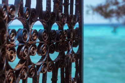 Close-up of metal fence by sea against sky