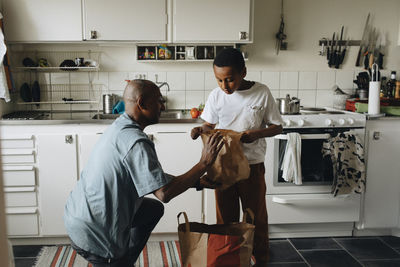 Father and son searching in paper bags in kitchen at home