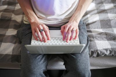 Midsection of man using laptop while sitting on bed at home