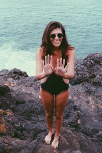 Young woman wearing sunglasses standing on rock at sea shore