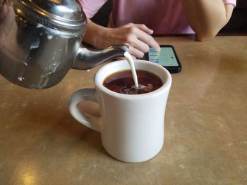 Close-up of hand pouring tea cup on table