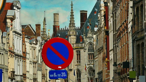 Road sign by buildings in city against sky