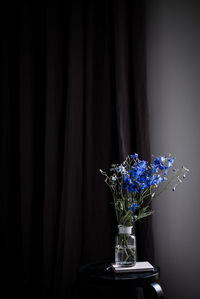 Blue flowers in vase on table against curtain