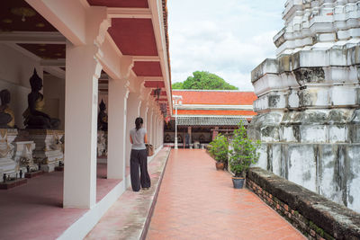 Rear view of female tourist walking near the old pagoda and buddha statues in the temple