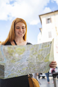 Pretty red hair woman is smiling alone looking at a paper city map