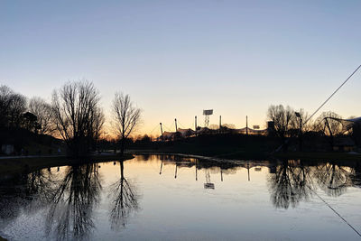 Reflection of bare trees in lake against clear sky