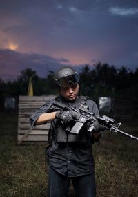 Rear view of man standing on field against sky during sunset with weapons and equipment at night