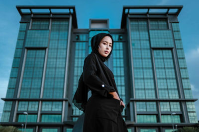 Portrait of young woman standing against building 