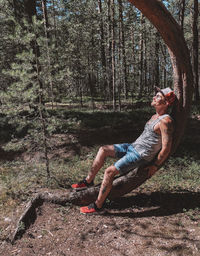 Side view of man sitting on tree trunk in forest