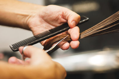 Cropped hand of hairdresser trimming hair at saloon