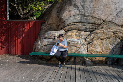 A middle-aged asian woman looking at her telephone in front of a massive rock