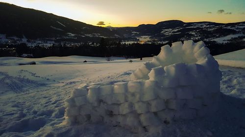 Snow covered landscape against sky during sunset