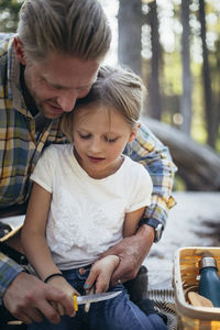 Father helping daughter in cutting stick in forest