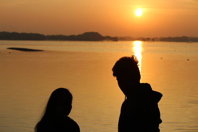 Silhouette friends standing against sea during sunset