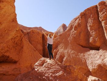 Rear view of man standing on rock formation against clear sky