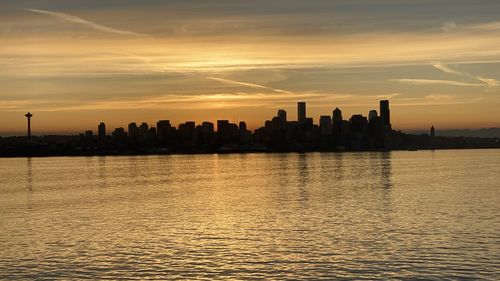 Silhouette buildings by sea against sky during sunset