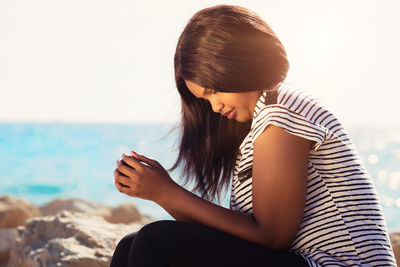 Young woman sitting on beach against sky