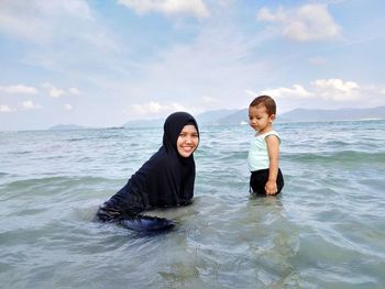Portrait of smiling woman with boy in sea against sky