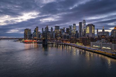 Illuminated buildings by river against sky at dusk