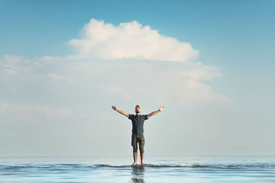 Man standing with arms outstretched at beach against sky