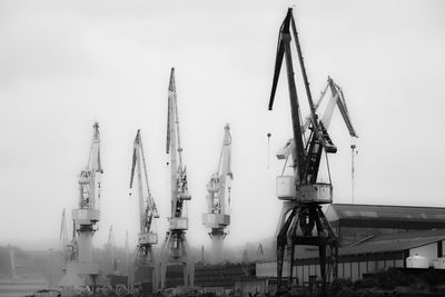 Cranes at harbor against clear sky