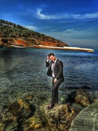 Man standing on rock by sea against sky