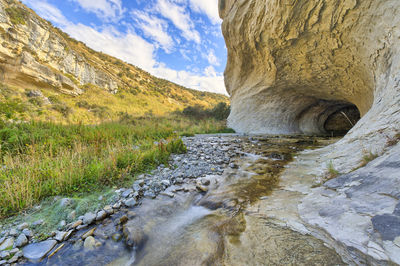 Stream flowing through rocks against sky