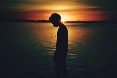 Silhouette of boy standing on beach at sunset